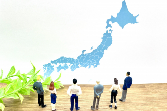 日本地図を見つめる人々のミニチュアと人口動態のイメージ