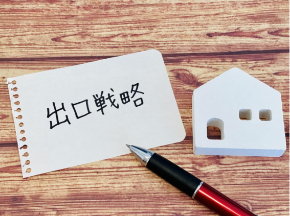出口戦略と書かれたメモと住宅模型、ペンのイメージ