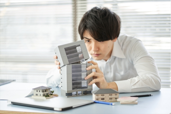 「建物模型を組み合わせて不動産投資を検討する男性のイメージ