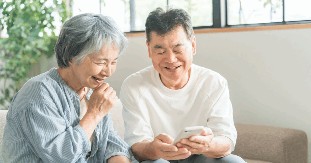 スマートフォンで見守りサービスを利用し安心して笑顔を見せる高齢夫婦